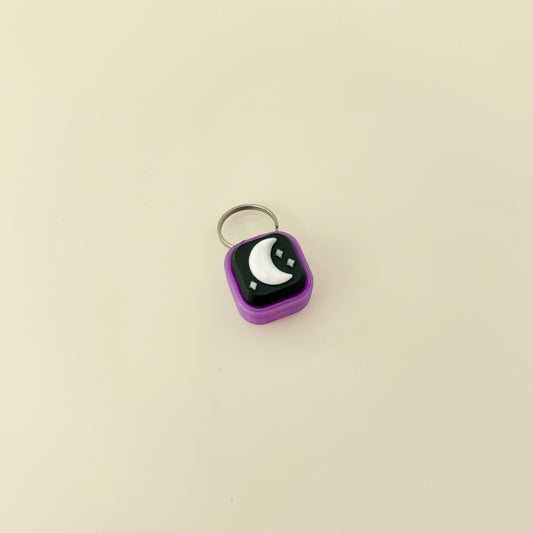 Small purple square keychain with a black and white design on a beige background