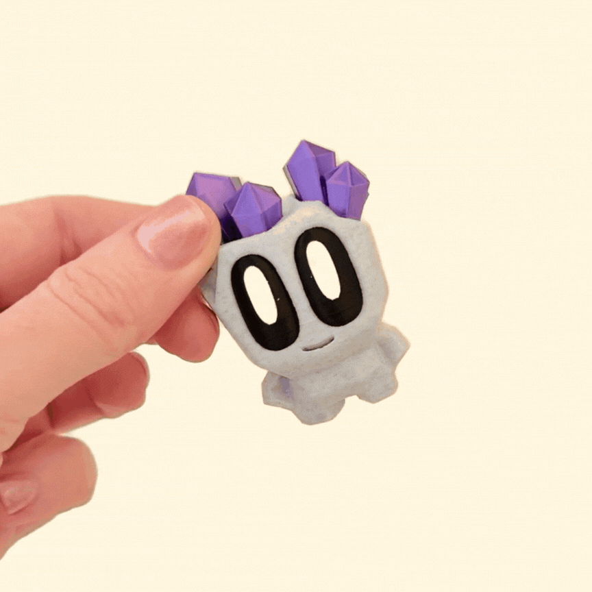 A shiny grey pet rock with metallic purple crystal details and big black and white eyes, paired with a brown crate.