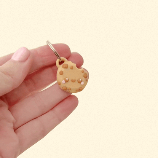 A fun cookie-shaped keyring with a smiling face and chocolate chips, attached to a silver ring.