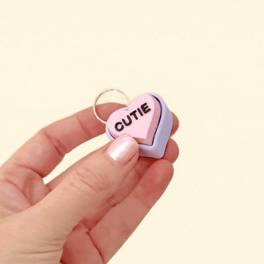 A heart-shaped fidget clicker on a keyring featuring a lilac and pink design with customisable messages.