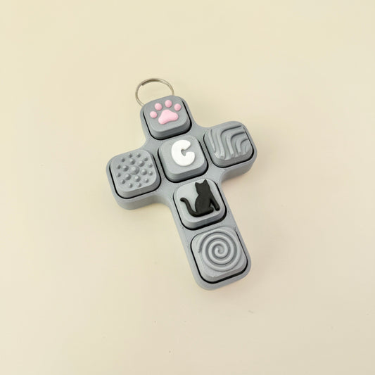 Gray cross-shaped fidget toy with various textured buttons on a beige background