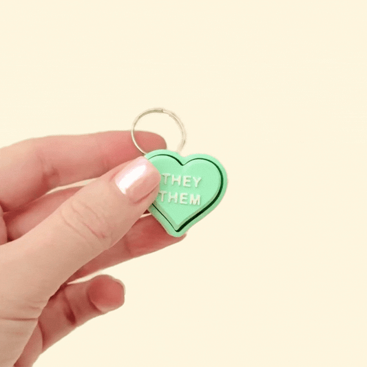 Mint green heart fidget clicker with personalised pronoun options, attached to a keyring.