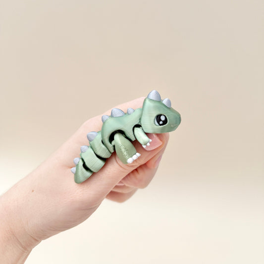 Shiny metallic green dinosaur fidget toy with silver spikes and black and white eyes.
