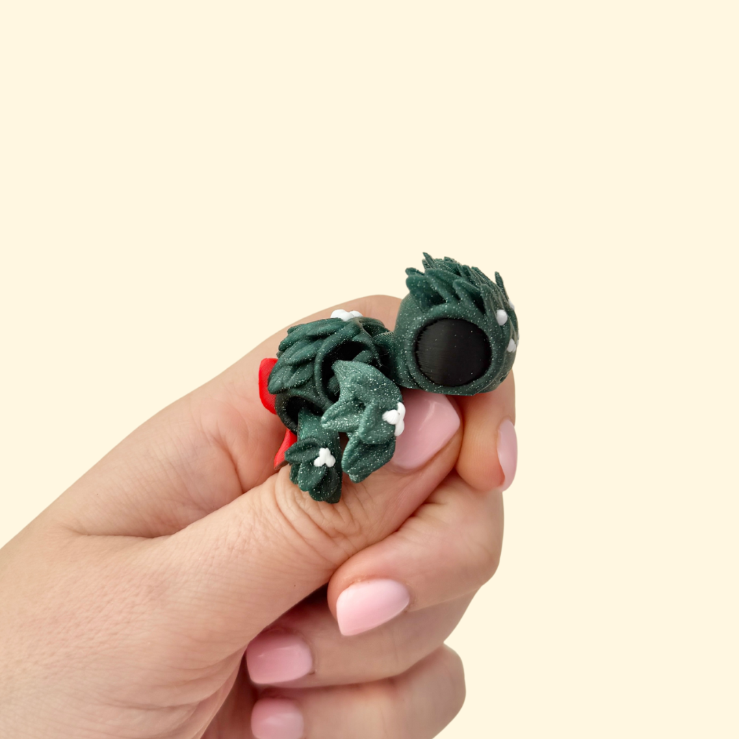 Small evergreen glitter turtle with leaf-textured body, red bow, and white berry dots, 5 cm festive fidget.