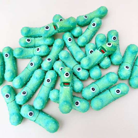 A shimmering green pickle-shaped toy with a single eye and an opening mouth for sensory play.