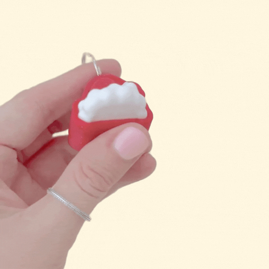 Tiny festive clicker with glossy red finish and raised accents for sensory input; lightweight and portable.