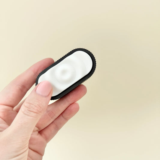 Sensory Ripple Click in black and white with ripple-textured clicker surface and ridged grip.