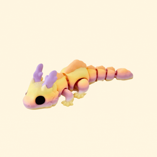 Skyburst Dragon fidget toy with sunrise tones of lilac, yellow, and orange, peach scales, and big black eyes.