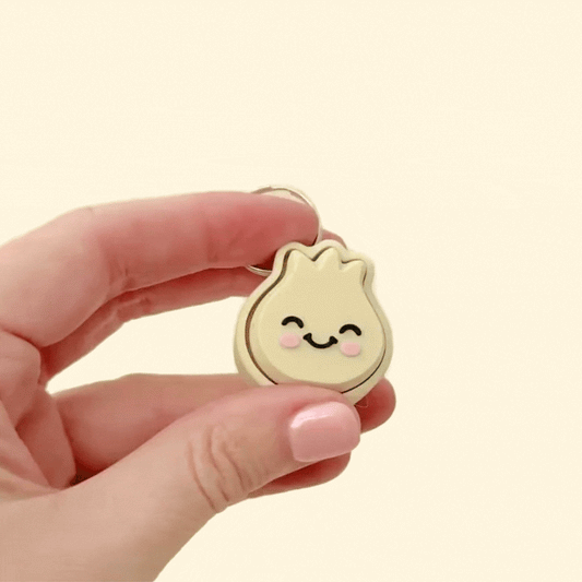 A beige dumpling clicker with a smiling face and pink cheeks, perfect for sensory play, stress relief, and keychain attachment.