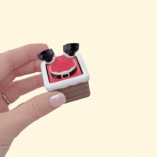 Holiday fidget clicker with snow-topped chimney and Santa legs; tactile brick texture, compact 5 cm size.