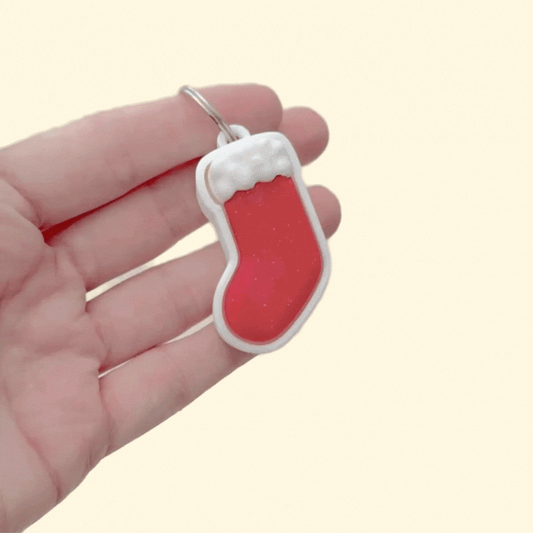 Holiday stocking-shaped clicker, smooth press surface with textured cuff for contrast; pocket-size stim tool for neurodivergent users.