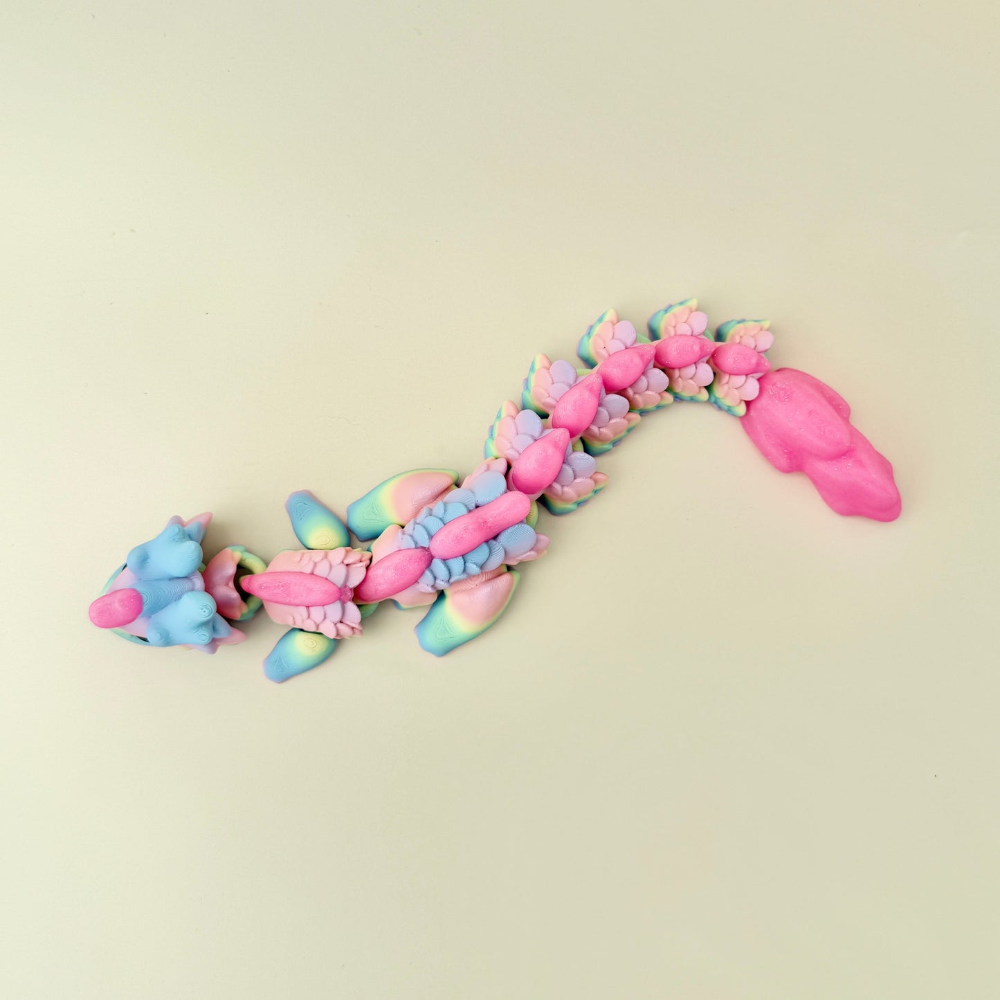 An articulated rainbow dragon fidget toy with shimmering pink accents along the head and back, designed for sensory engagement.