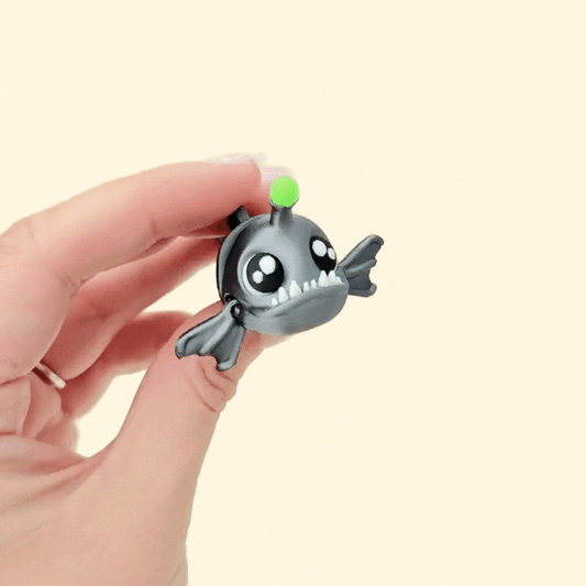 Shiny black and silver angler fish fidget toy with lime green glow and sharp white teeth