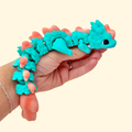 Articulated dragon fidget in aqua with coral spikes; textured scales; quiet, smooth movement for calming stims.
