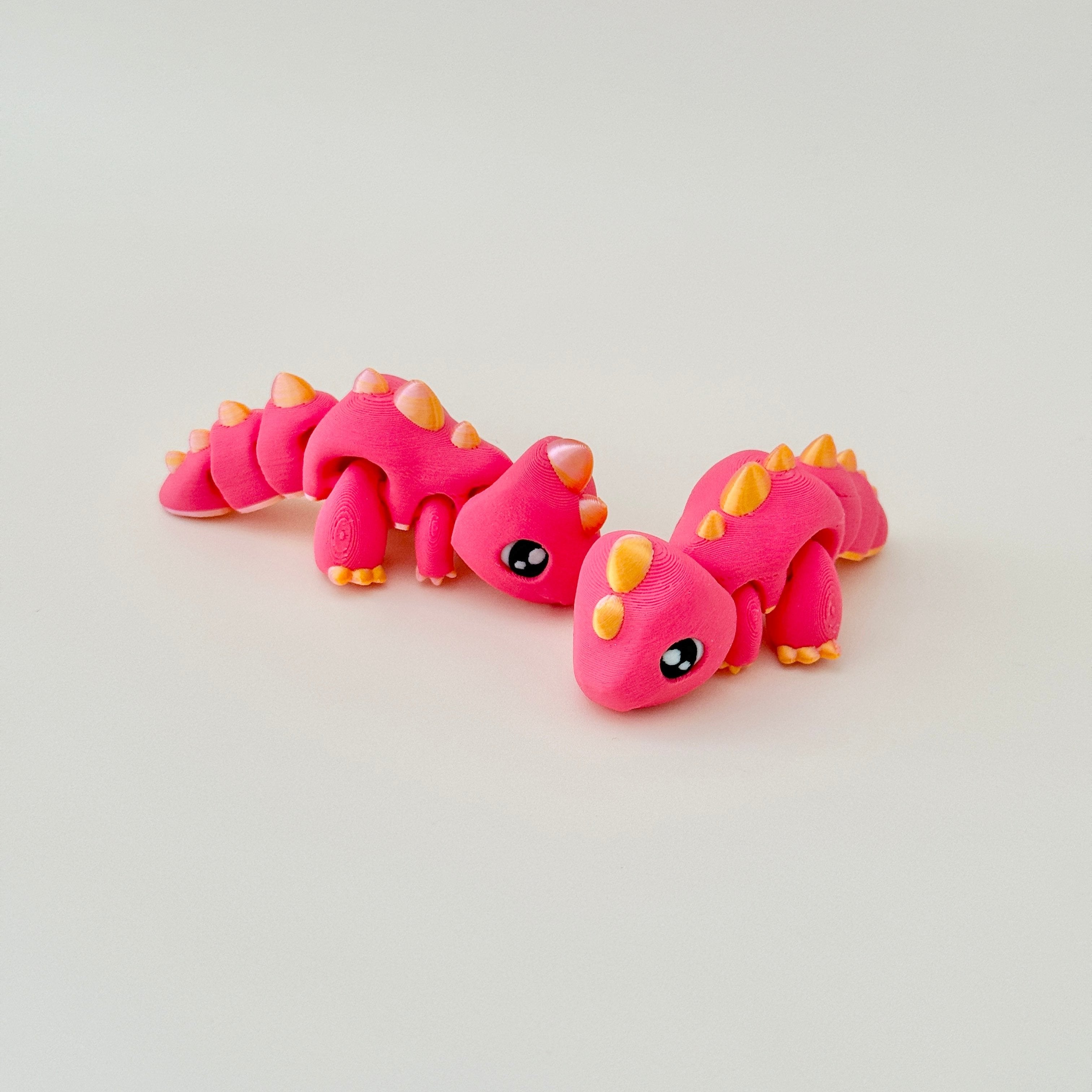 A small dinosaur fidget toy in red with shiny gold accents, designed for standing or lying flat.