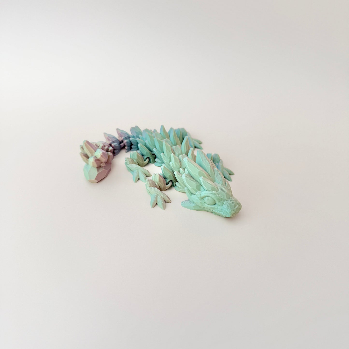 Fully articulated Baby Crystalborne Dragon fidget toy in colour-changing filament, available in red, blue, and gold or green, gold, and pink.