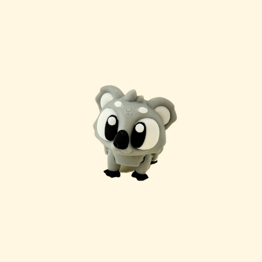 Mini articulated baby koala fidget toy featuring grey and black colouring and large, expressive black-and-white eyes.