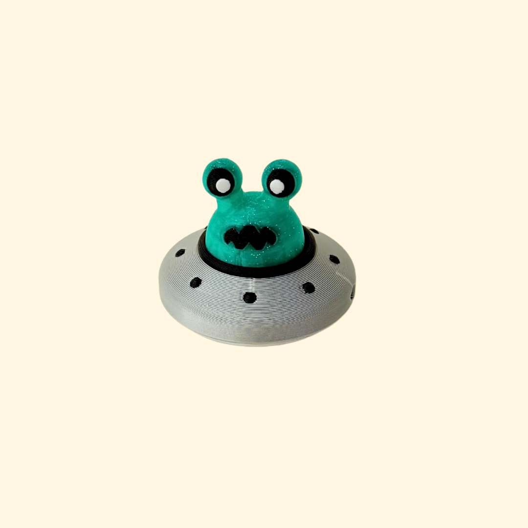 Glittery green alien head press-down clicker in a silver UFO saucer.
