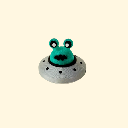Glittery green alien head press-down clicker in a silver UFO saucer.
