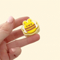 A small, yellow and brown bee-shaped fidget clicker toy with white wings.