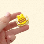 A small, yellow and brown bee-shaped fidget clicker toy with white wings.
