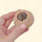 A handheld novelty clicker with raised texture and a central press button for repetitive fidgeting.
