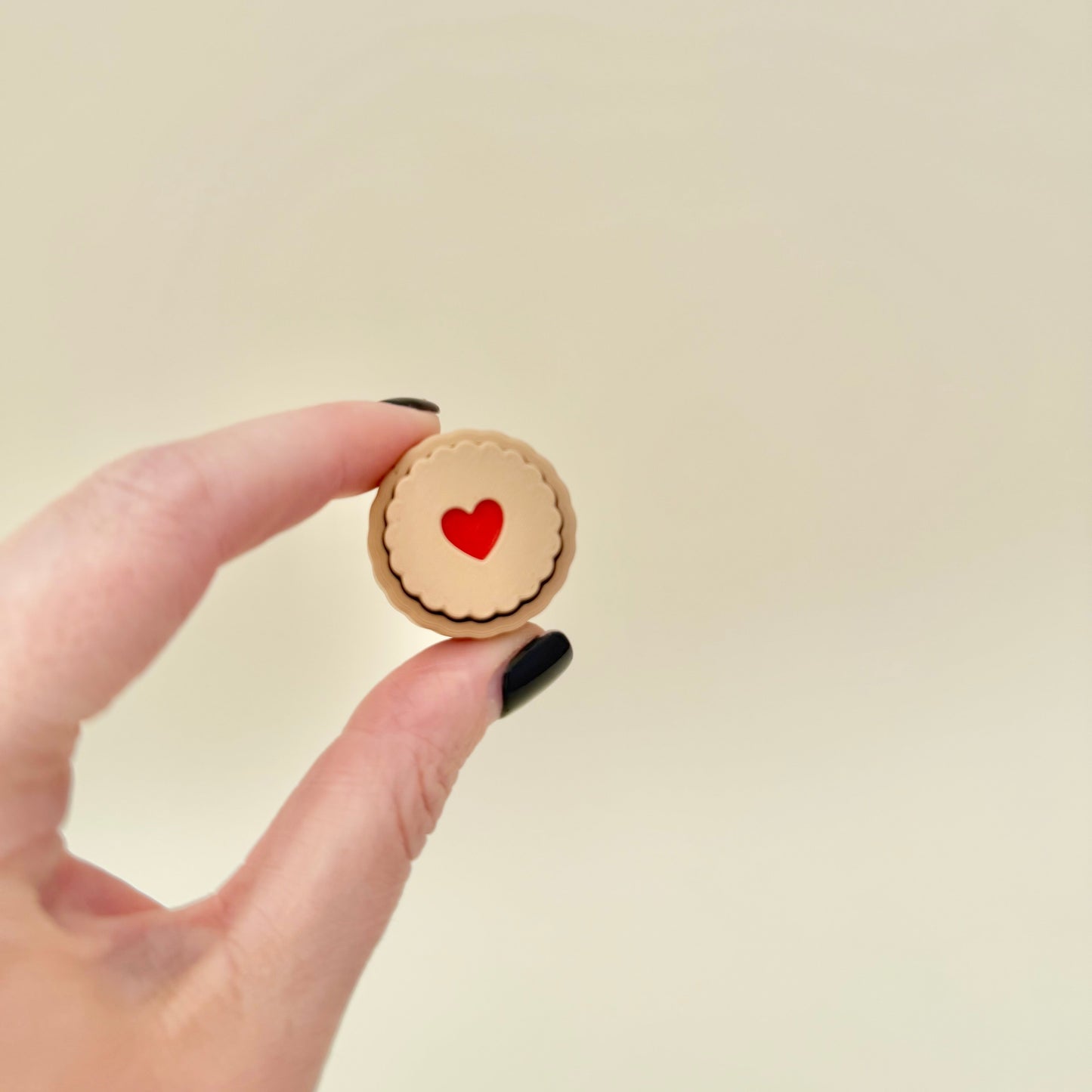 Mini biscuit fidget with scalloped edge and red centre, 3 cm, press-to-click mechanism, available in heart or tree design, sensory friendly.
