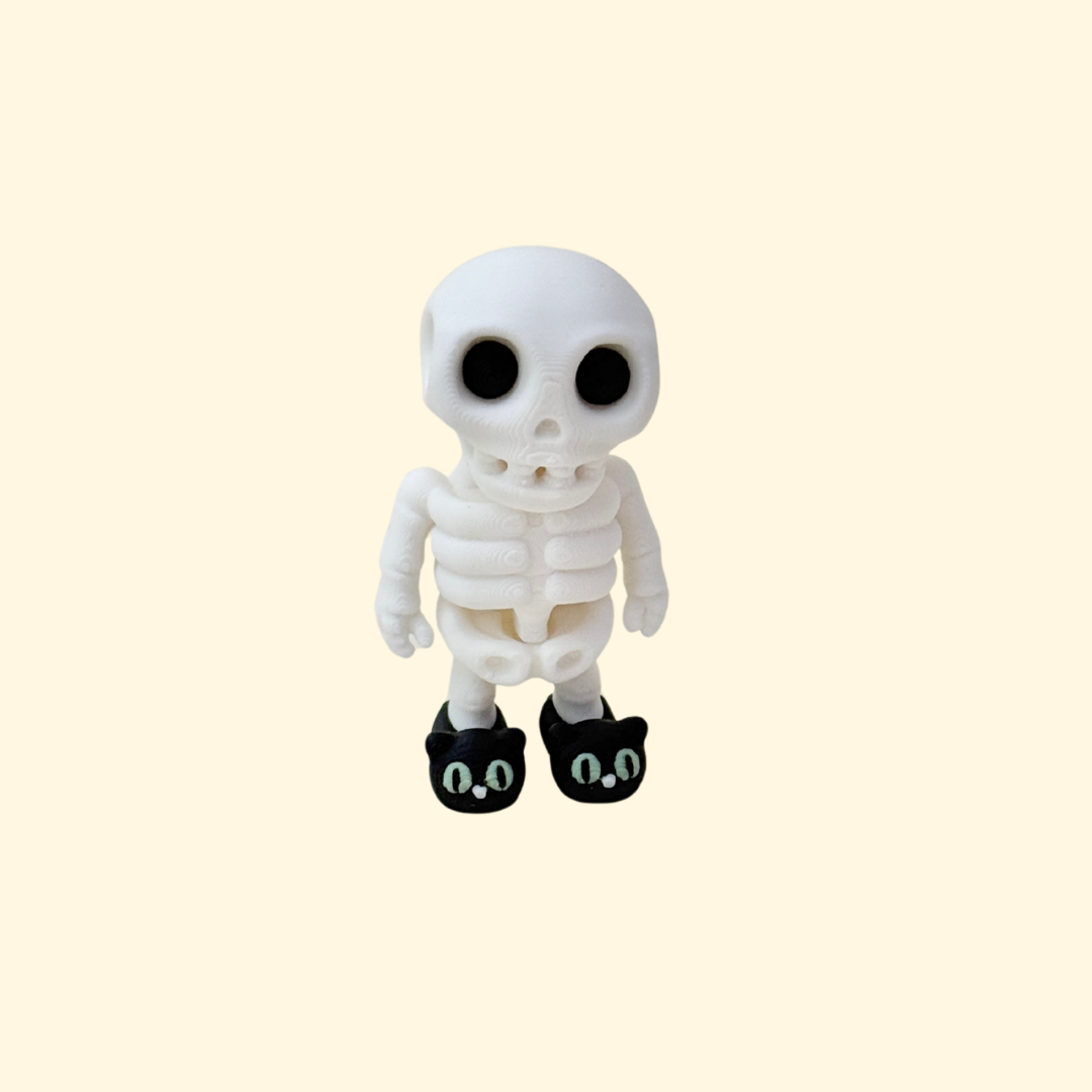 Small articulated skeleton with black cat slippers and glow-in-the-dark eyes that stands on a desk.
