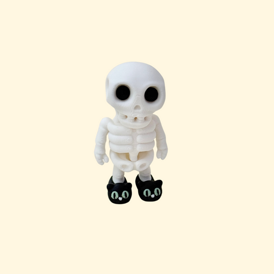 Small articulated skeleton with black cat slippers and glow-in-the-dark eyes that stands on a desk.
