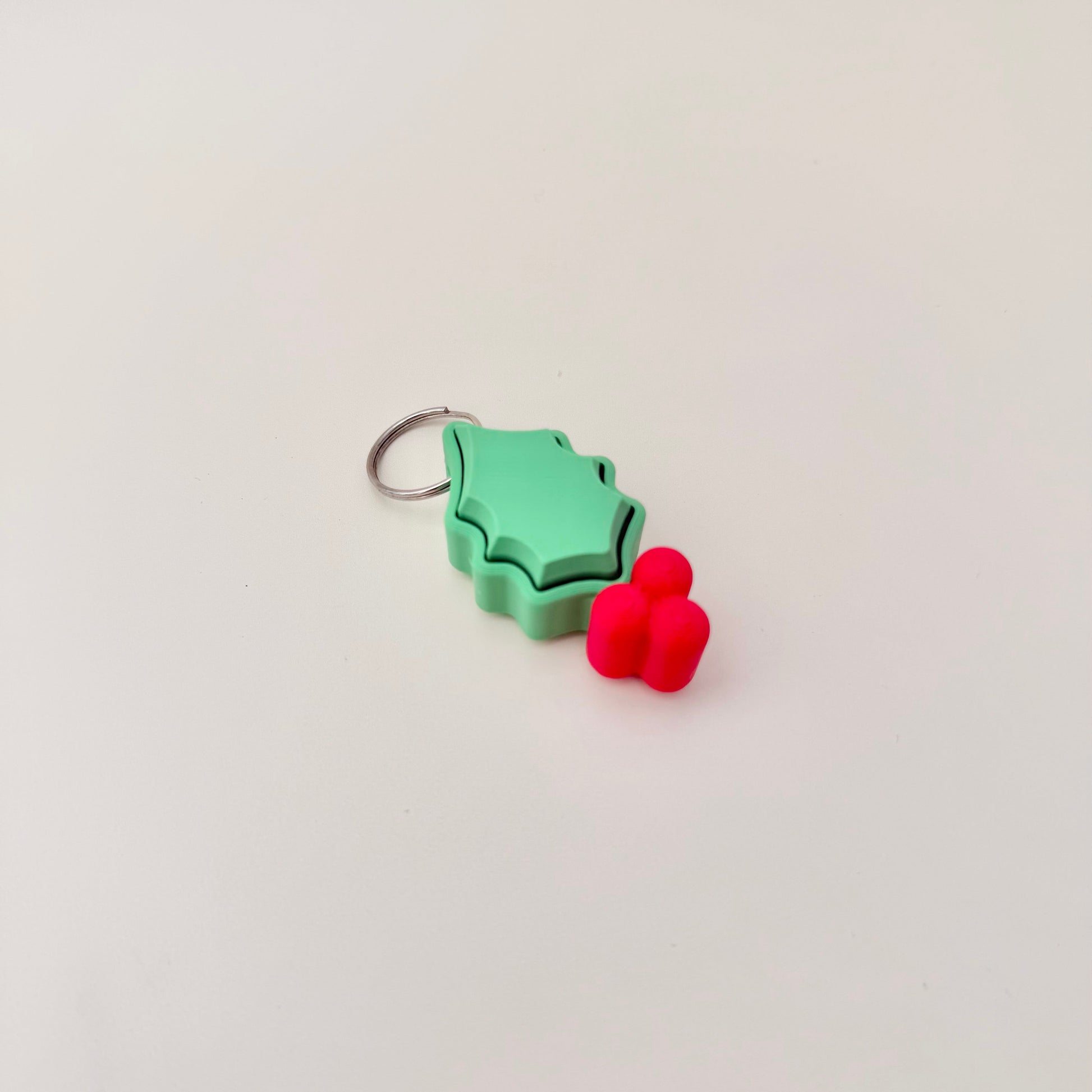 Green holly leaf clicker with berries, 5 cm, attaches to keys or bags, optional quiet click.
