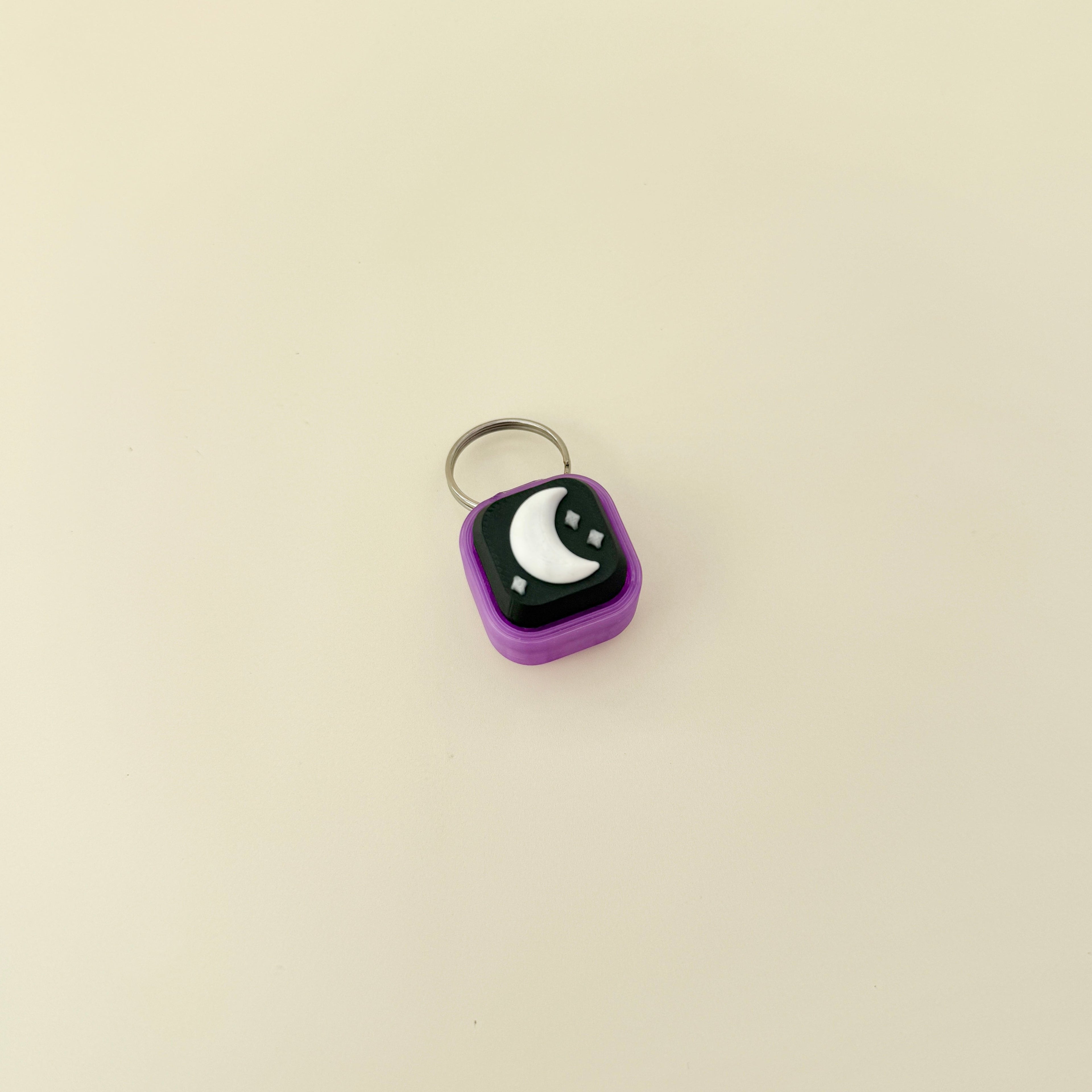Small purple square keychain with a black and white design on a beige background