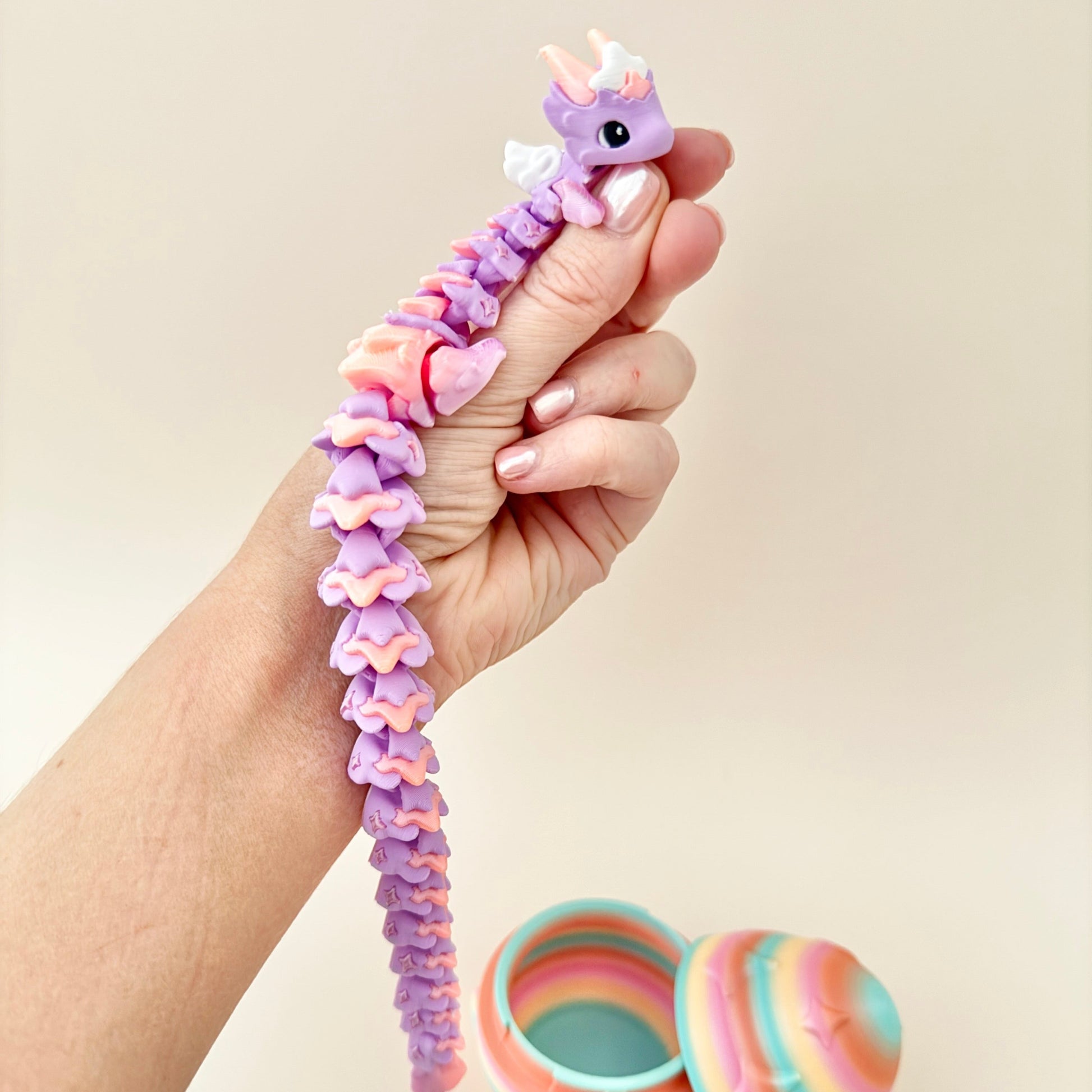 Whimsical fidget dragon with lilac and peach tones and a twinkling rainbow egg.