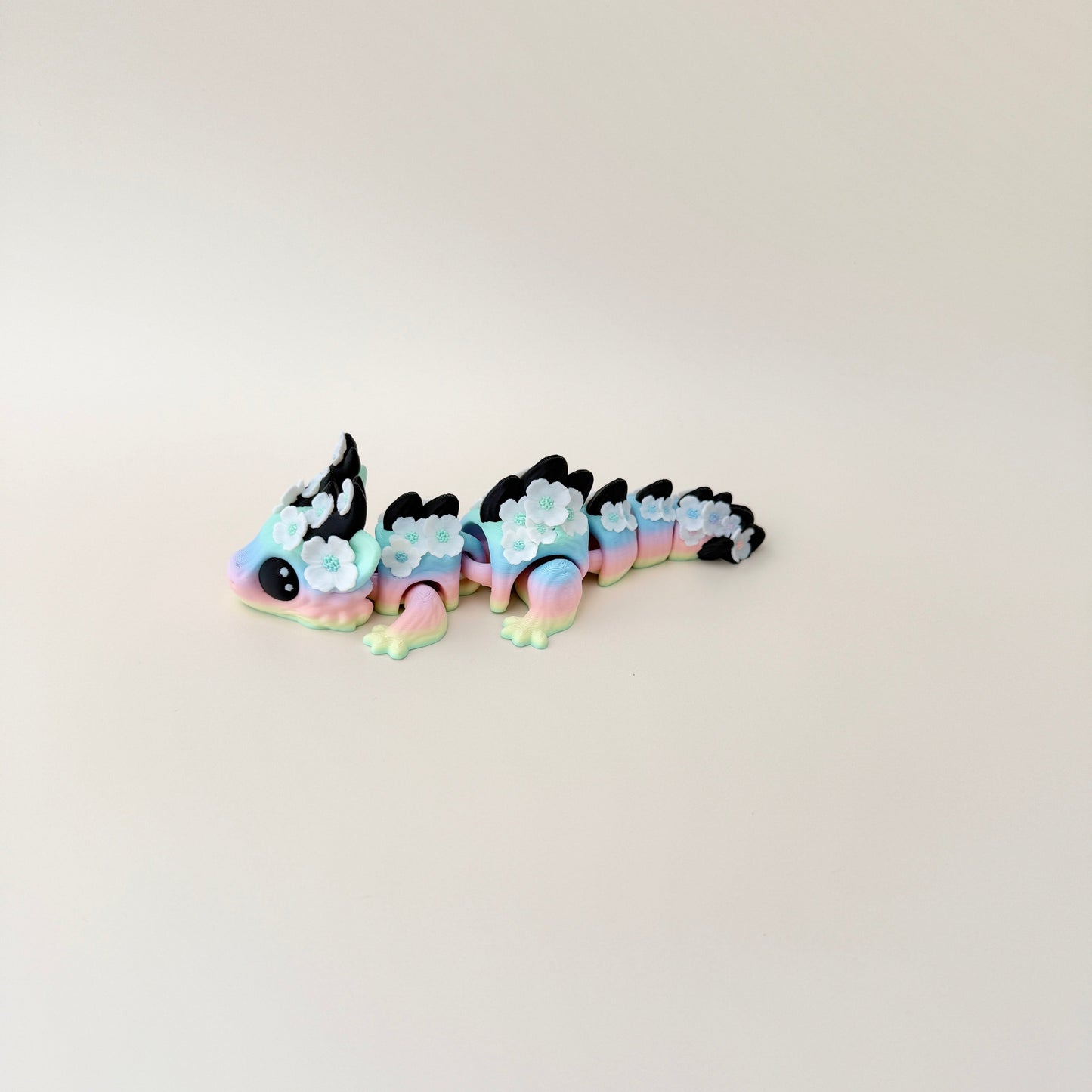 Collectable dragon fidget toy with a pastel rainbow body, white flowers, and black spiky details.