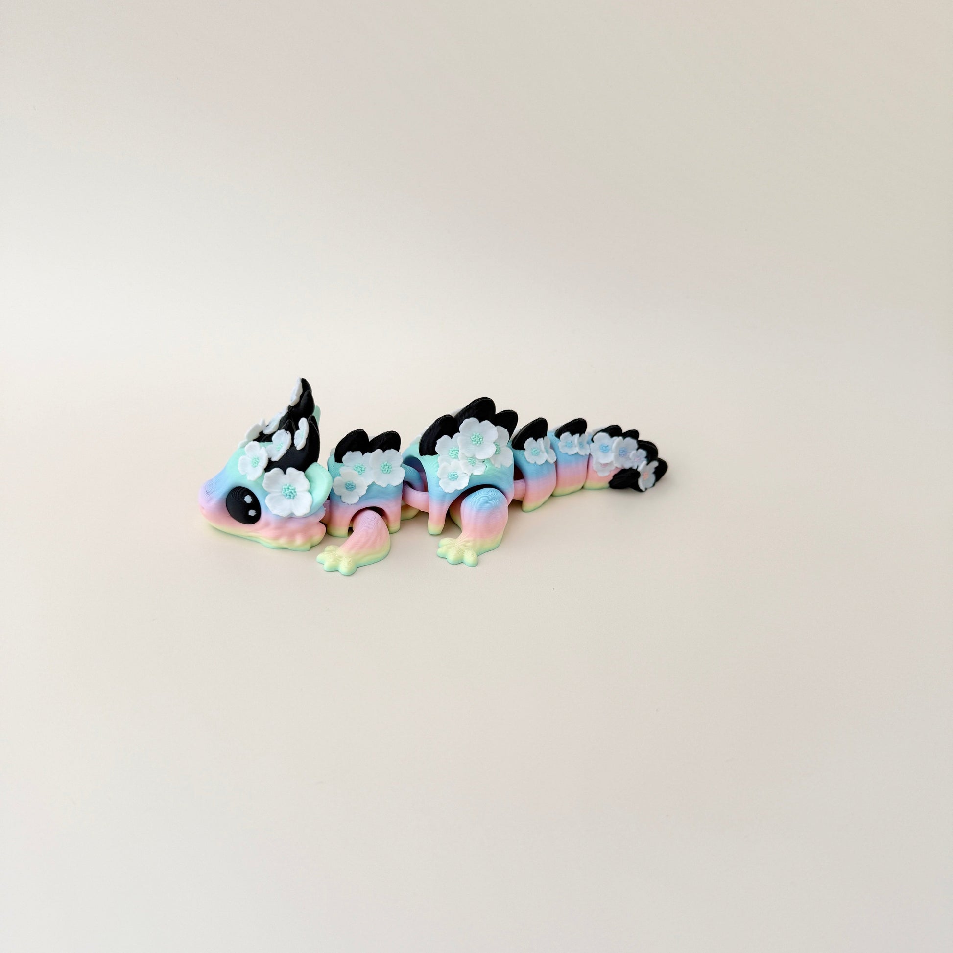 Collectable dragon fidget toy with a pastel rainbow body, white flowers, and black spiky details.