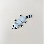 Mottled grey, white, and black raccoon fidget toy that stands up or lies down.