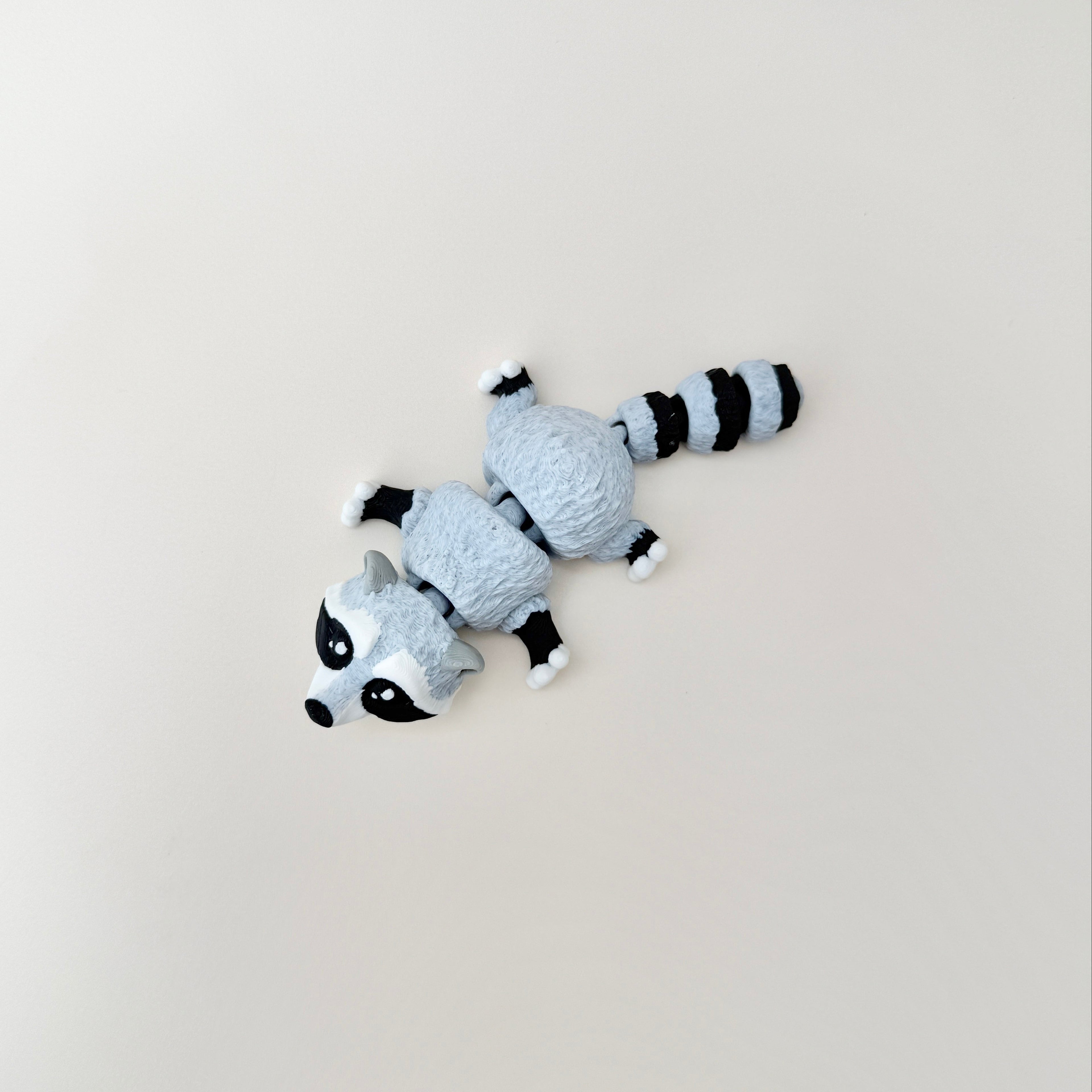 Mottled grey, white, and black raccoon fidget toy that stands up or lies down.