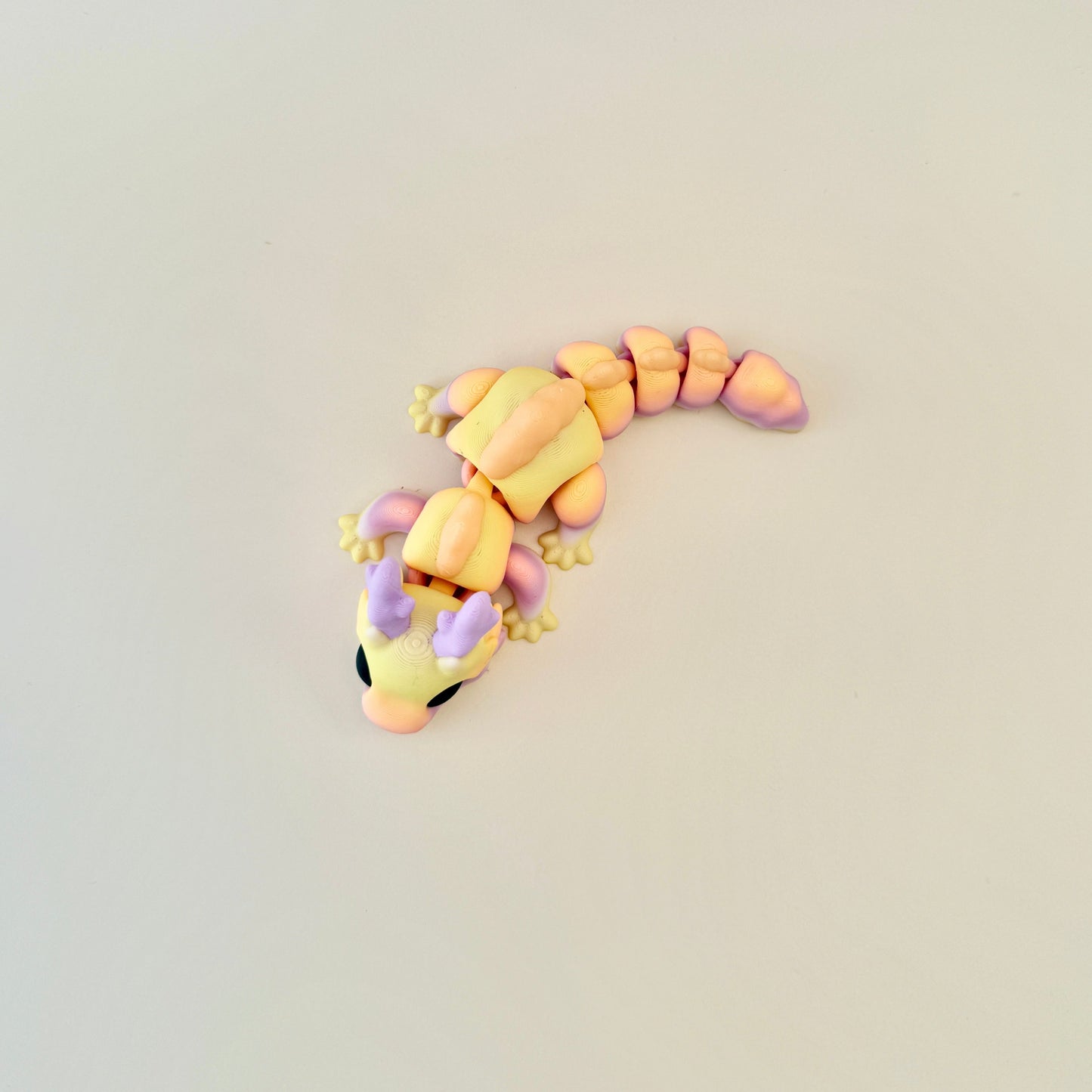 Dragon fidget toy with lilac, yellow, and orange tones, complemented by peach scales and lifelike black eyes.