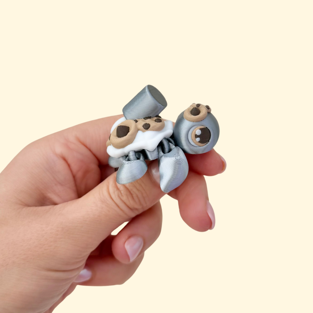 Metallic silver articulated turtle with cookie textures and milk splash on shell, 5 cm desk-friendly sensory fidget.

