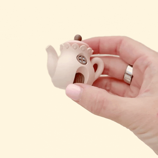 Mini teapot-shaped fidget with a press-to-click lid and neutral cottage details.
