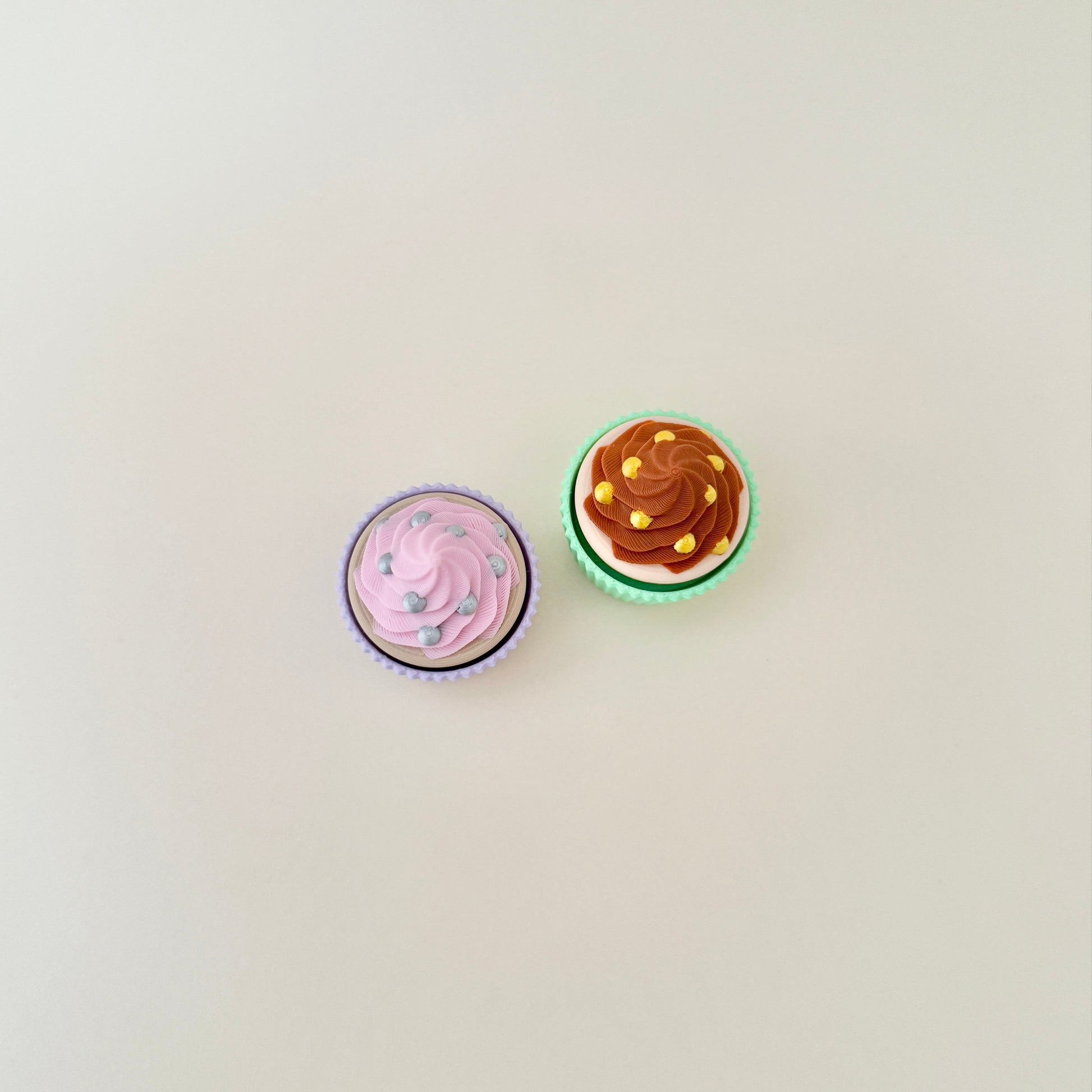 Pink and chocolate cupcake clickers side by side, showcasing their adorable frosting and sprinkle designs.