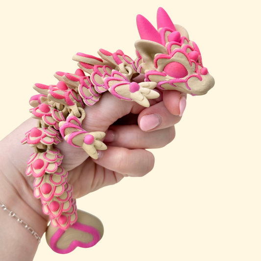 Fully articulated biscuit style dragon with pink piped icing texture and heart details, Valentine fidget toy.
