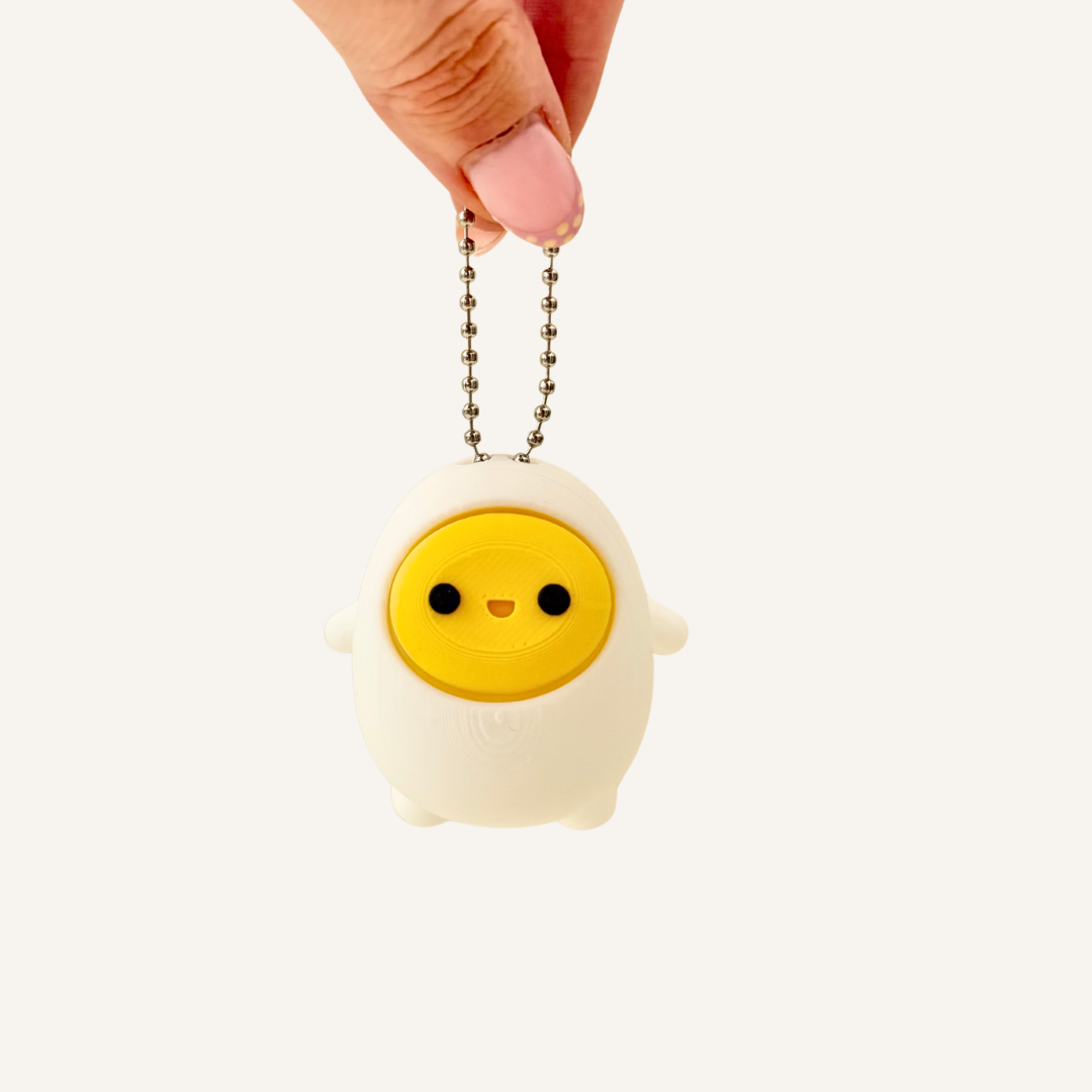 Palm-sized egg keyring fidget with yolk press button, available in click or quiet click for portable sensory play.
