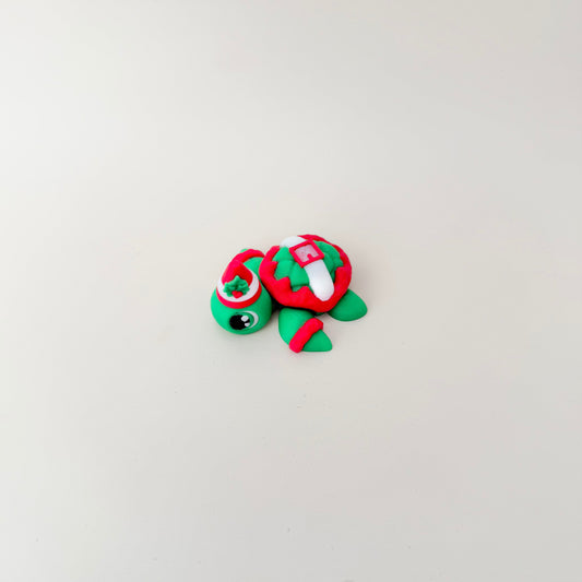 Christmas turtle fidget, 5 cm articulated with textured shell and hat, red and green colours, palm-size sensory toy for pockets or desks.
