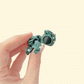 Tiny dark-green turtle figurine with textured leaves and a bright red bow; pocket-size holiday desk pal.
