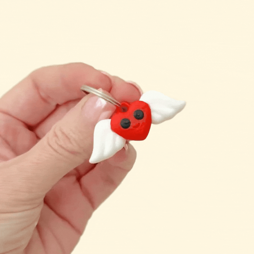 A vibrant red heart keyring with black eyes, a smile, and white moving wings.