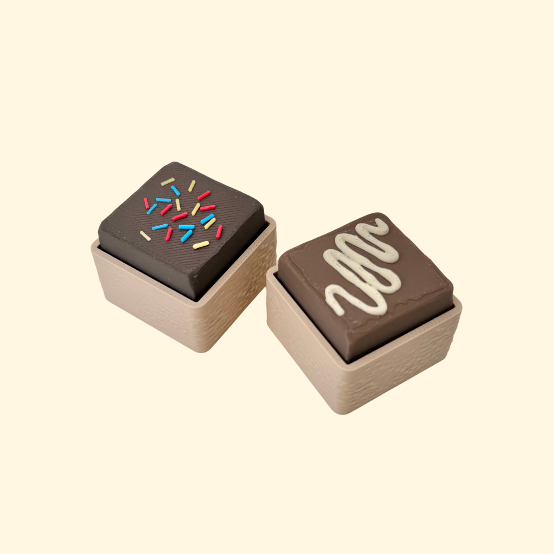 Mini fudge clicker fidget with sprinkles or drizzle top, pocket-sized, satisfying press, optional quiet click upgrade.
