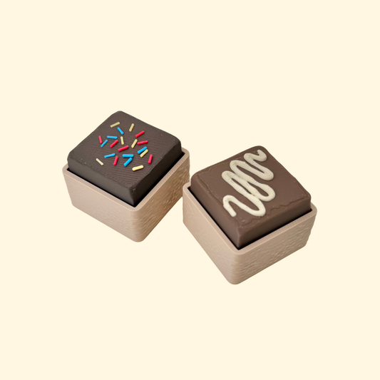 Mini fudge clicker fidget with sprinkles or drizzle top, pocket-sized, satisfying press, optional quiet click upgrade.
