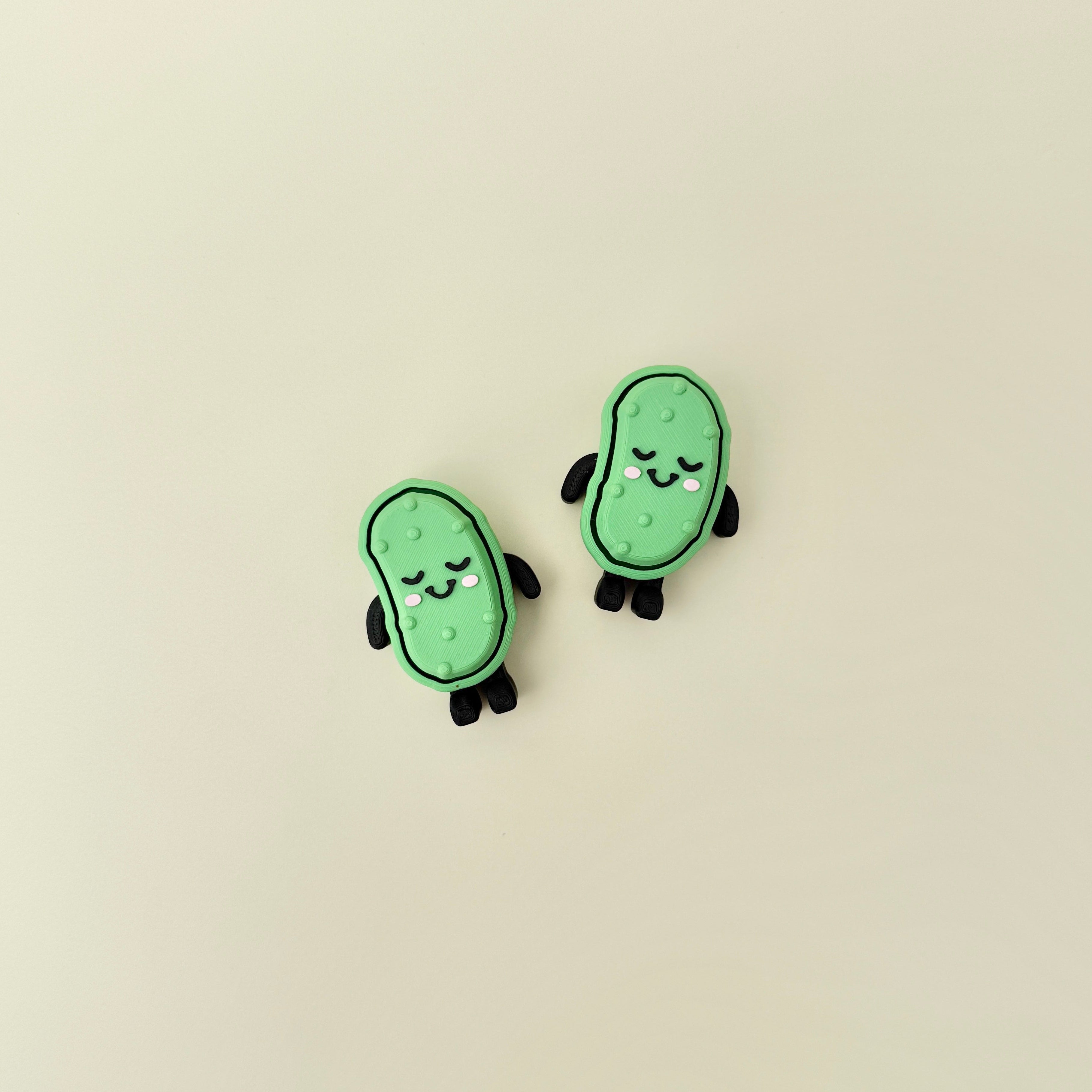 Compact pickle-shaped stim toy with face, limbs, and a firm press-to-click top.