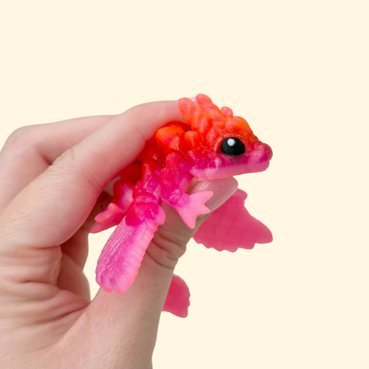 Small articulated dragon fidget with wings, heart details, and a glitter red and pink finish.
