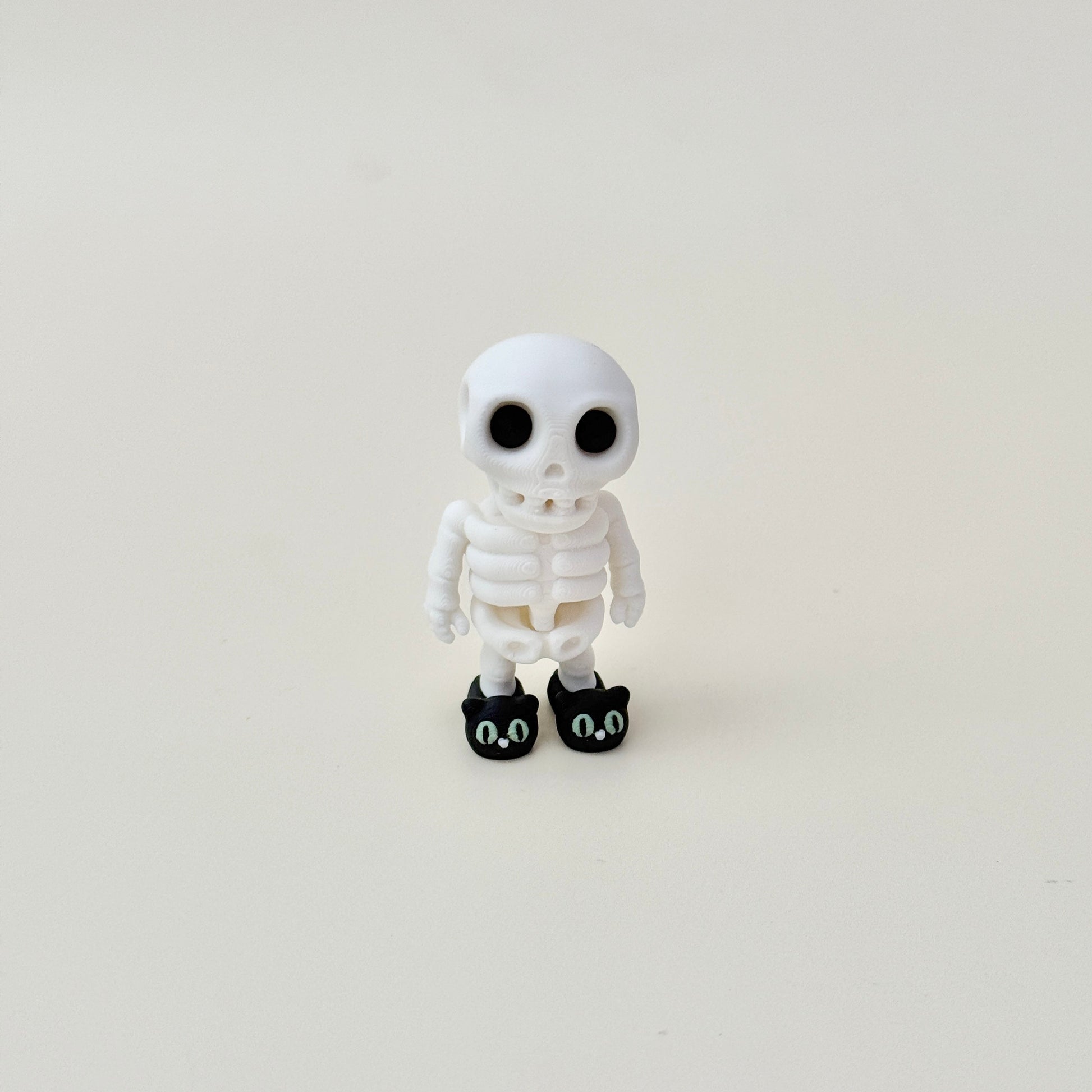 Black cat slippers on a white skeleton with luminous eyes for a playful spooky touch.
